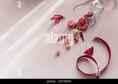 Autumn composition from ribbon and wineglass full of red dried flowers and leaves Stock Photo