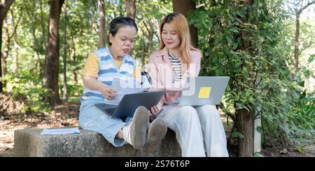 Diverse friends reviewing project materials together outdoors in a peaceful park, supported by technology Stock Photo
