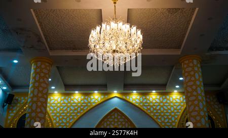 A beautifully designed interior featuring a large crystal chandelier hanging from a textured ceiling. The walls are adorned with intricate golden patt Stock Photo