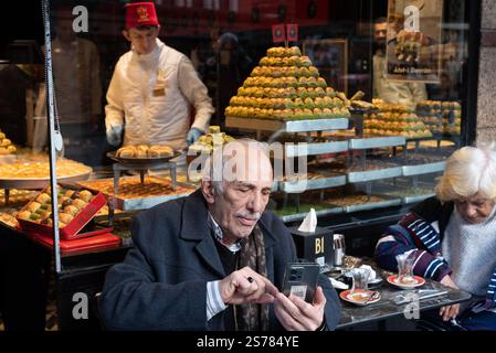 Istanbul, Turkey. 08th Jan, 2025. An elderly gentleman using his mobile phone outside a Turkish sweetshop in a central shopping district of Istanbul. With an ever expanding population in excess of 15 million people, Istanbul is the largest city in Turkey; spanning the continents of Europe and Asia is a dynamic economic and cultural hub and the former historical capital. Credit: SOPA Images Limited/Alamy Live News Stock Photo