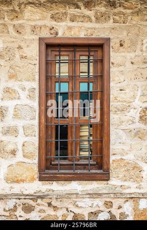 Rustic wooden window with bars on stone wall. Stock Photo