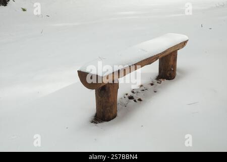 a handmade bench made of wooden logs covered with snow in Etna Park, Sicily, Italy Stock Photo