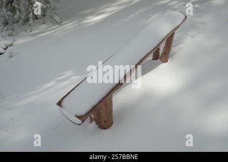 a handmade bench made of wooden logs covered with snow in Etna Park, Sicily, Italy Stock Photo