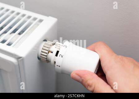 Person is adjusting the temperature on a radiator. The radiator is white and has a knob on it Stock Photo