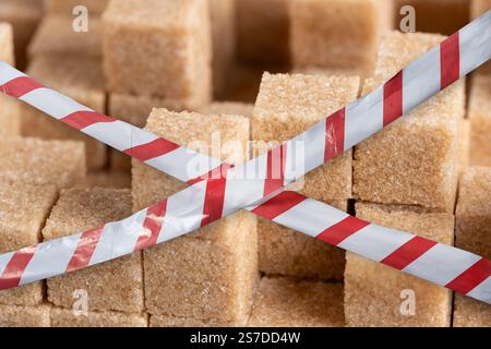 Cubes cane sugar with red and white warning tapes, closeup Stock Photo