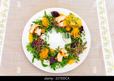 A vibrant salad features arugula, grilled chicken, various vegetables, and cheese. It is artistically arranged on a white plate, creating an appealing Stock Photo