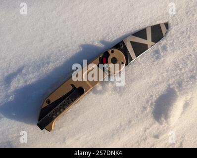Folding tactical knife on white snow. Stock Photo