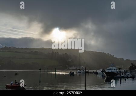Sun breaking through grey clouds and mist over East Portlemouth with sunrays cutting through, taken from Salcombe harbour wall. Stock Photo