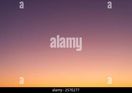 Clear sunset sky background. Vibrant gradient from orange to purple. Beautiful and natural color transient without any clouds. Real sky view. Stock Photo