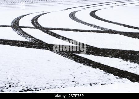 Close-up of vehicle tire tracks creating intersecting patterns on snow-covered ground during winter season, showcasing texture and wintertime themes. Stock Photo