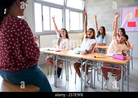 Portrait of happy group diverse elementary school students sitting in classroom with hands raised.  Stock Photo