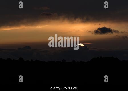 Dramatic sunset, black and yellow, sun almost hidden behind the clouds Stock Photo