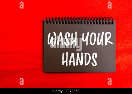 Wash your hands message written on black notebook page with red background. Conceptual wash your hands symbol. Copy space. Stock Photo