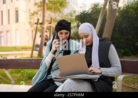 Muslim businesswomen working remotely using laptop and smartphone in a park Stock Photo