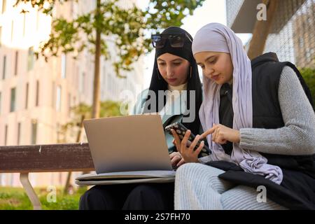 Two muslim businesswomen working outdoors with laptop and smartphone Stock Photo