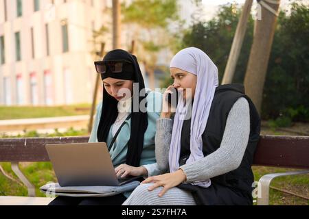 Two muslim businesswomen working remotely on a laptop and smartphone in a park Stock Photo