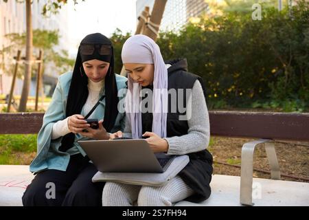 Two muslim businesswomen working remotely on a park bench Stock Photo