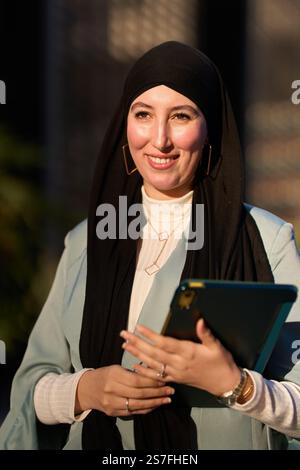 Smiling muslim businesswoman holding tablet and wearing hijab Stock Photo