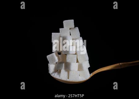 White cubes sugar and granulated sugar in spoon on black background, close up. The concept of unhealthy eating, obesity, heart disease, diabetes Stock Photo