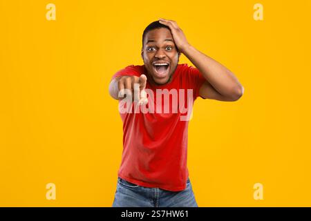Excited African Guy Pointing Finger At Camera Laughing, Yellow Background Stock Photo