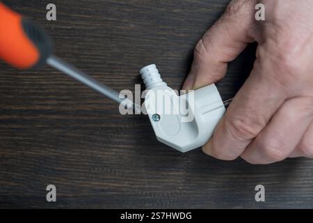Using a Phillips screwdriver, loosen the screw on the white electrical power plug, close up. The process of parsing the body of plastic electrical plu Stock Photo