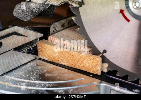 Blade of a miter saw to cut off the edge of a wooden board, close up. Working on a circular saw in a workshop Stock Photo
