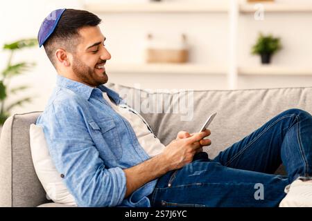 Smiling jew man using mobile phone sitting on couch Stock Photo