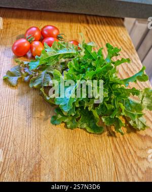Fall harvest fresh organic salad ingredients grape tomatoes and spring mix lettuce on a vintage wooden cutting board.  Vertical view. Stock Photo