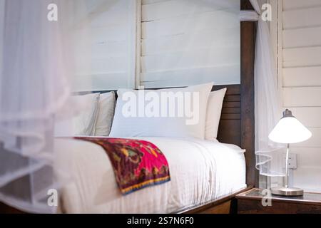 Bedroom with mosquito net tied to bedpost. Table lamp on side table. Holiday or vacation concept. Stock Photo