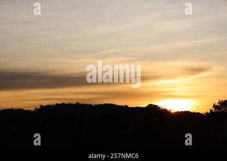 sunrise above rain forest covered hills paints high thin clouds pastel hues of pink orange gold blue gray mauve purple Stock Photo