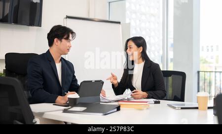 Two businesspeople are meeting in a meeting room, having a nice conversation. A beautiful, positive Asian businesswoman is working with her male colle Stock Photo