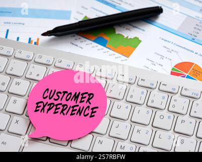 Pink sticky note labeled customer experience placed on a computer keyboard with charts and graphs in the background Stock Photo