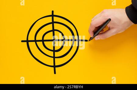 Hand drawing a target on a vibrant yellow background, representing the pursuit of success and the achievement of key goals or objectives. Goal design. Stock Photo