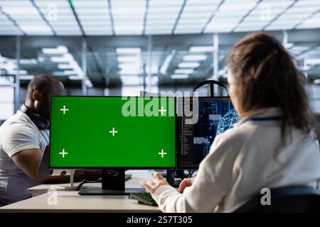 Isolated screen PC in front of IT support workers upgrading AI equipment. Engineers at PC desk overseeing artificial intelligence server clusters using chroma key computer Stock Photo