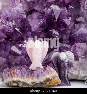 Rose quartz and amethyst angel shape figurines against amethyst geode crystal indoors, studio shot. Spiritual home decor concept. Stock Photo