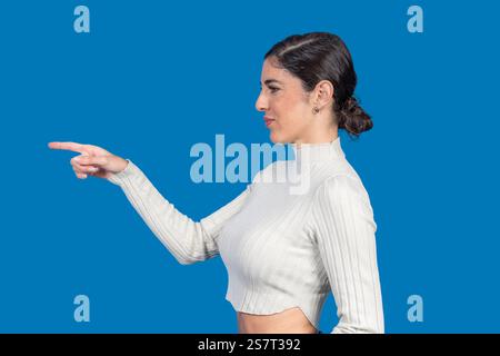Side view of young woman pointing with index finger to the left on blue background Stock Photo