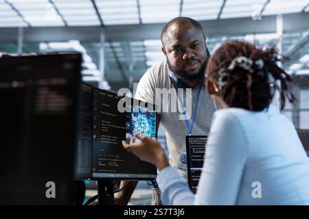 System administrator working with colleague in data center facility providing computing resources for different workloads. IT expert talking with coworker while monitoring AI supercomputers Stock Photo