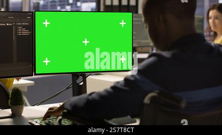 Man with disability in inclusive workplace working with machine learning tech on green screen computer. African american IT expert with paraplegia in wheelchair works with data on mockup PC, camera A Stock Photo