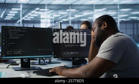 Overworked engineer falling asleep while typing on computer in server hub, monitoring data center energy consumption. Tired technician struggling to stay awake while inspecting rackmounts, camera B Stock Photo