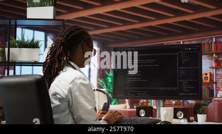 Programmer types code into PC, entering commands, running script. African american IT professional in apartment fixing errors in application, implementing new features, camera A Stock Photo