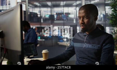 Upbeat software engineer utilizing cloud computing resources to train and deploy large scale machine learning models. Jolly man monitoring company systems, ensuring their reliability, camera B Stock Photo