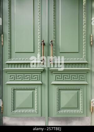 Light green door of an old house. Entrance to 19th century building - classical style wooden door with decorations, brass colored handles and hinges. Stock Photo