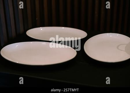 Three elegant oval white plates on a dark surface. Stock Photo