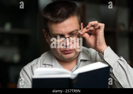 Adult handsome smiling man in glasses reading book while sitting Stock Photo