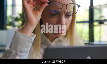 Embarrassed Caucasian woman businesswoman girl in eyeglasses looking at laptop computer overwork female office worker manager take off spectacles Stock Photo