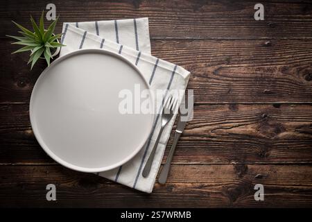 Top view of empty ceramic white plate, fork and table knife on wooden table Stock Photo