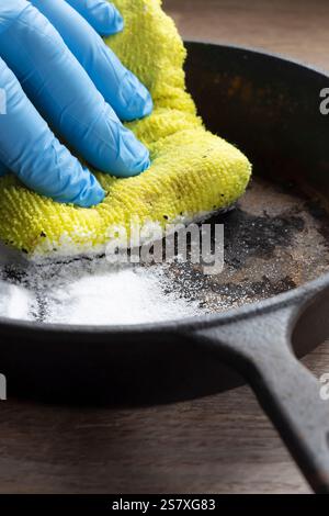 Person cleaning a rusty old cast iron frying pan using bicarbonate of soda and a scouring pad. On a wood board background. Stock Photo