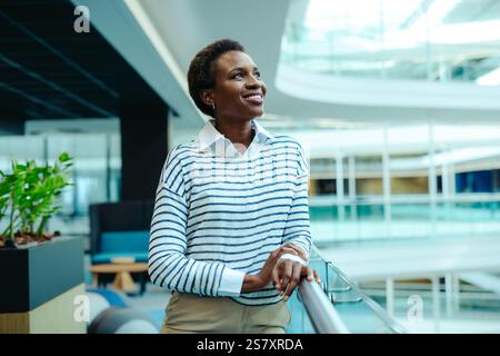A confident female professional stands in a modern office environment, wearing a striped sweater and smiling warmly. The contemporary setting suggests Stock Photo