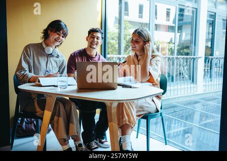 Three high school friends gather in the library, engaging in a video call while studying at a round table, showcasing camaraderie and collaborative le Stock Photo
