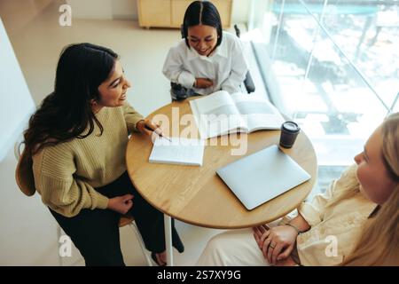 Three students collaborate over textbooks and laptops, engaged in a productive study session. The setting emphasizes teamwork, education, and school s Stock Photo
